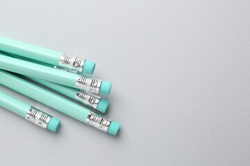 Many graphite pencils with erasers on light grey background, flat lay. Space for text