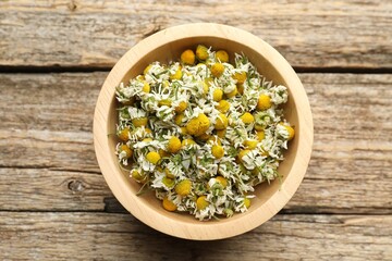 Dry chamomile flowers in bowl on wooden table, top view