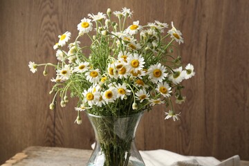 Beautiful chamomile flowers in glass vase on table, closeup