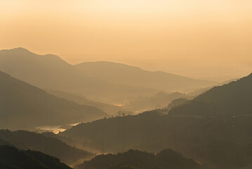 Golden hour light illuminating misty mountain ranges and valleys with a serene river, natural...