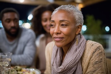 A reflective woman enjoys a quiet moment at a dinner table, illuminated by soft lights, enhancing the intimate ambiance and feelings of connection with her companions.