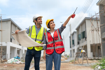 Civil male engineer holding blueprints and Asian female architect with walkie talkie working...
