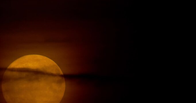 Telescopic timelapse of a full moon rising and glowing through a dark sky until it fades out