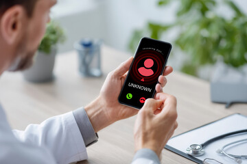 A person in a white coat receives an incoming call from an unknown caller on a smartphone at a desk with medical tools.