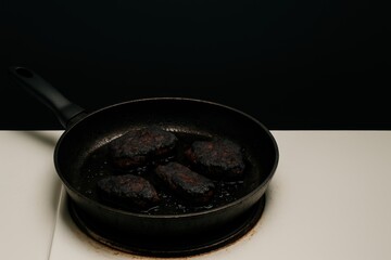 Blackened meat cooking in a skillet on a dark background with frying oil