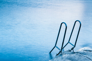 Ladder leading into calm Swedish coastal waters invites exploration during serene daylight
