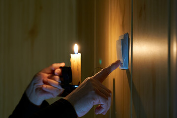 A man with a burning candle in his hand turns a light switch on and off. Blackout no electricity...