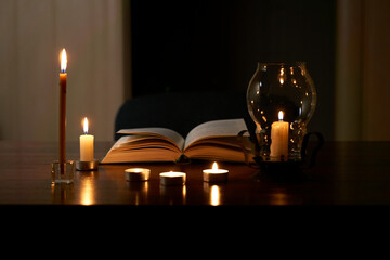 Book and burning candles on table in dark room. Blackout. Problems with power supply
