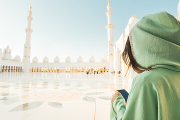 Sheikh Zayed Grand Mosque tour excursion or booking a visit concept.Female tourist visitor hold use phone post online travel photo check social media . Awe of iconic Islamic architecture in Abu Dhabi