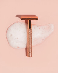 Rose gold safety razor on pink background with shaving cream texture swipe