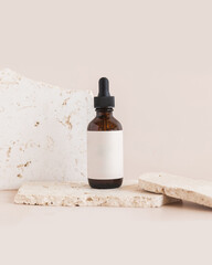 Glass amber dropper bottle on tan background with natural stones and blank label