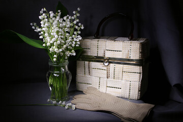 A bouquet of lilies of the valley, a white bag and gloves lie on the table