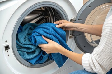 Close-up of a woman putting blue wool clothes into a washing machine.