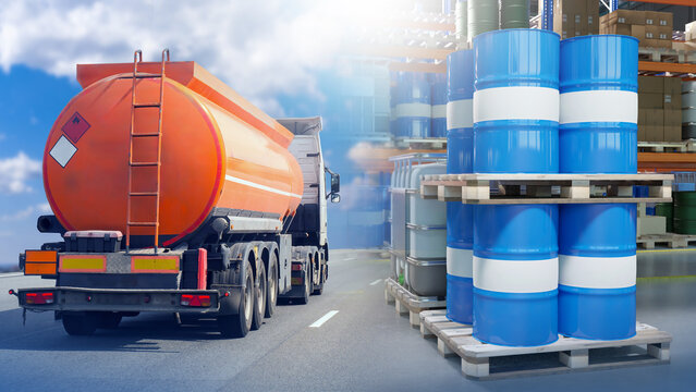 Fuel tanker truck transporting flammable liquid passes by pallets of chemical barrels at industrial warehouse. Activity: Chemical transport, hazardous materials logistics.