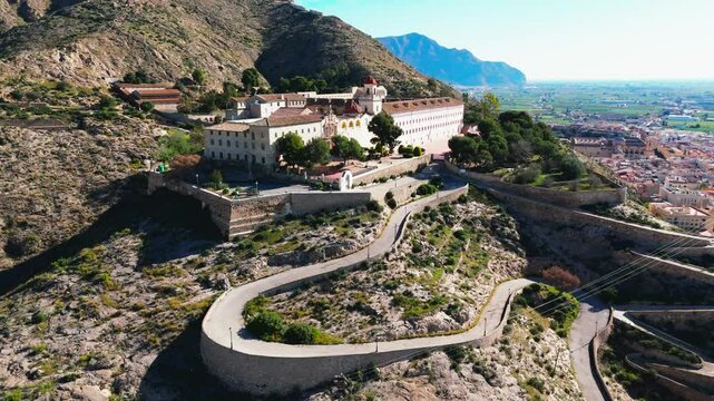 Aerial view of curvy road goes up hill of San Miguel Diocesan Seminary complex atop rugged hill overlooking Orihuela town, Spain. Costa Blanca, province of Alicante. Travel destination concept
