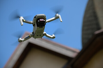 Drone in the air inspecting the roof over the house closeup blue sky background