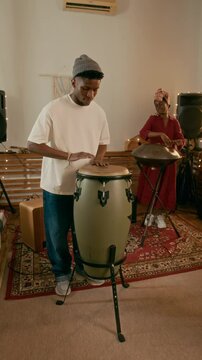 Vertical shot of young African American man in casual attire beating percussion against his girlfriend playing glucophone during musical repetition in home studio