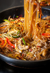Asian glass noodle stir-fry with chicken and vegetables in a rustic ceramic  bowl