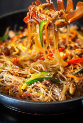 Asian glass noodle stir-fry with chicken and vegetables in a rustic ceramic  bowl
