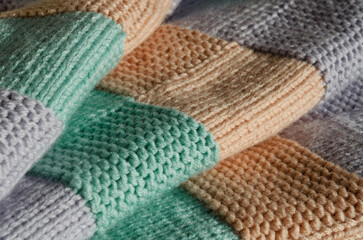 A close-up of a soft, hand-knitted throw blanket. The blocks of pastel colors are mint green, peach, and lilac.