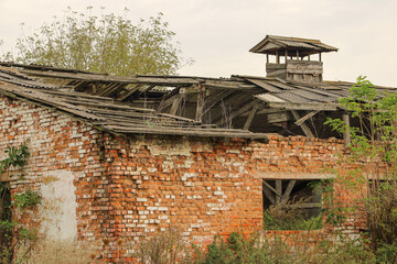 A partially destroyed brick building with a damaged roof, featuring a tower-like structure on top....