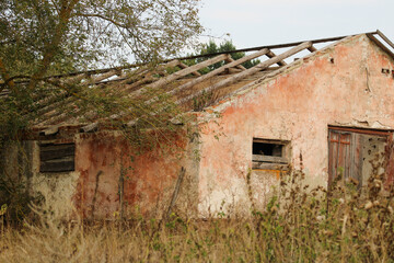 A building with a collapsed roof, surrounded by overgrown plants. The broken structure and scattered debris emphasize the effects of time and neglect	
