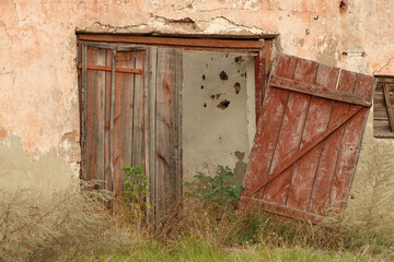 A partially open doorway leading into a deteriorated building. The structure's crumbling walls and vegetation creeping in highlight its abandoned state
