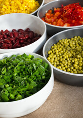 Close-up of several white and grey bowls filled with fresh, colorfully sliced ​​green onions,...