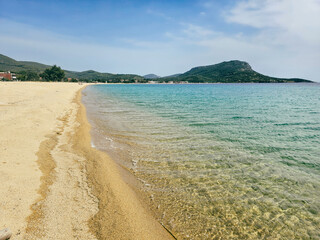 Yellow sand beach view with clear water and gentle waves under a blue sky in Toroni village on Sithonia peninsula, Greece