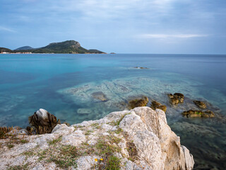 Calm turquoise waters and rocky shoreline at sunset near the coastal hills in Toroni on Sithonia peninsula, Greece