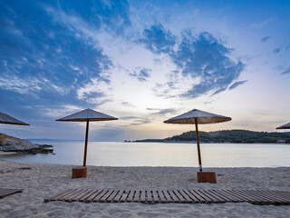 Tranquil beach at sunset with straw umbrellas overlooking the calm water and distant hills in Toroni on Sithonia peninsula, Greece
