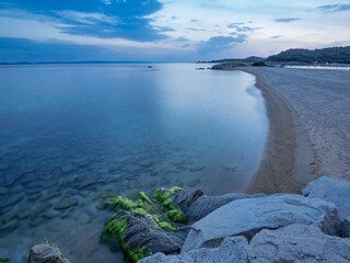 Calm evening at a coastal beach with smooth waves and rocky shoreline under a cloudy sky in Toroni on Sithonia peninsula, Greece