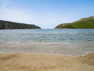 Serene coastline view with gentle waves and green hills under a clear sky during midday at Porto Koufo on Sithonia peninsula, Greece