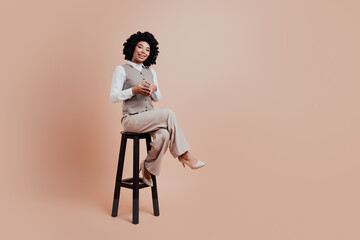 Confident young business professional woman in formal attire sitting on stool with beige...