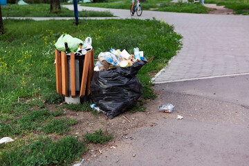 Overflowing green garbage bin in Surrey park clothe to Thames Path.