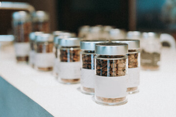 Modern Glass Jars with Coffee Beans and Blank Labels on White Surface