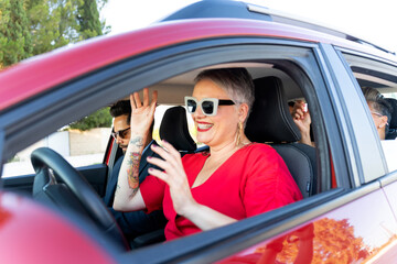 Bride leaving wedding in red car with friends waving goodbye