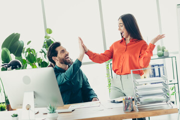 Cheerful coworkers sharing a high-five at a bright office workspace showcasing teamwork and...