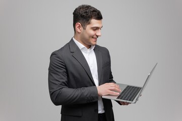Young professional in a suit smiles while using a laptop in a minimalist studio setting
