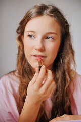 Naklejka premium Girl applying lipstick for a fun and creative makeup session at home during a bright afternoon