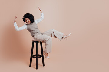 Businesswoman elegantly posing on a stool in beige formal attire on a matching background, vibrant...