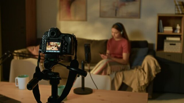 Professional camera on tripod recording video with teenager listening to music and writing ideas on paper