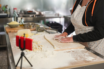 Italian senior woman doing homemade gnocchi while using mobile phone for live stream - Cooking class online concept