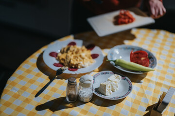 A bright and cozy scene of a breakfast table featuring assorted foods like cheese, peppers, and eggs against a checkered tablecloth.