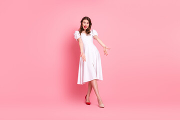 Young woman posing in white dress with playful gesture on vibrant pink background for fashion and lifestyle concepts