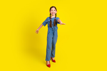 Cheerful young girl in stylish blue outfit posing playfully against a vibrant yellow background