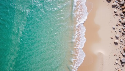 aerial view of a pristine beach with turquoise water gently lapping against pale sand, rocks on the shoreline, subject at the top with clear copy space at the bottom.