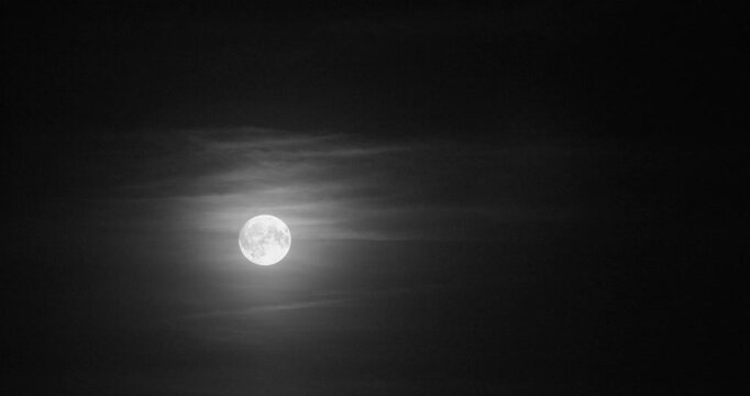 Mesmerizing timelapse of a glowing moon moving in dark sky with smooth clouds