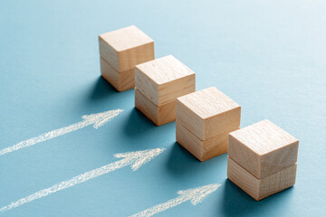 Wooden blocks stacked in ascending order on blue background, with chalk arrows symbolizing growth, progress, and upward trend, showcasing business success concept