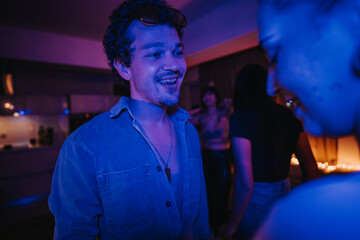 A group of friends enjoying a birthday party in a dimly lit room with vibrant lighting, creating a fun and festive atmosphere. Everyone appears to be having a great time.